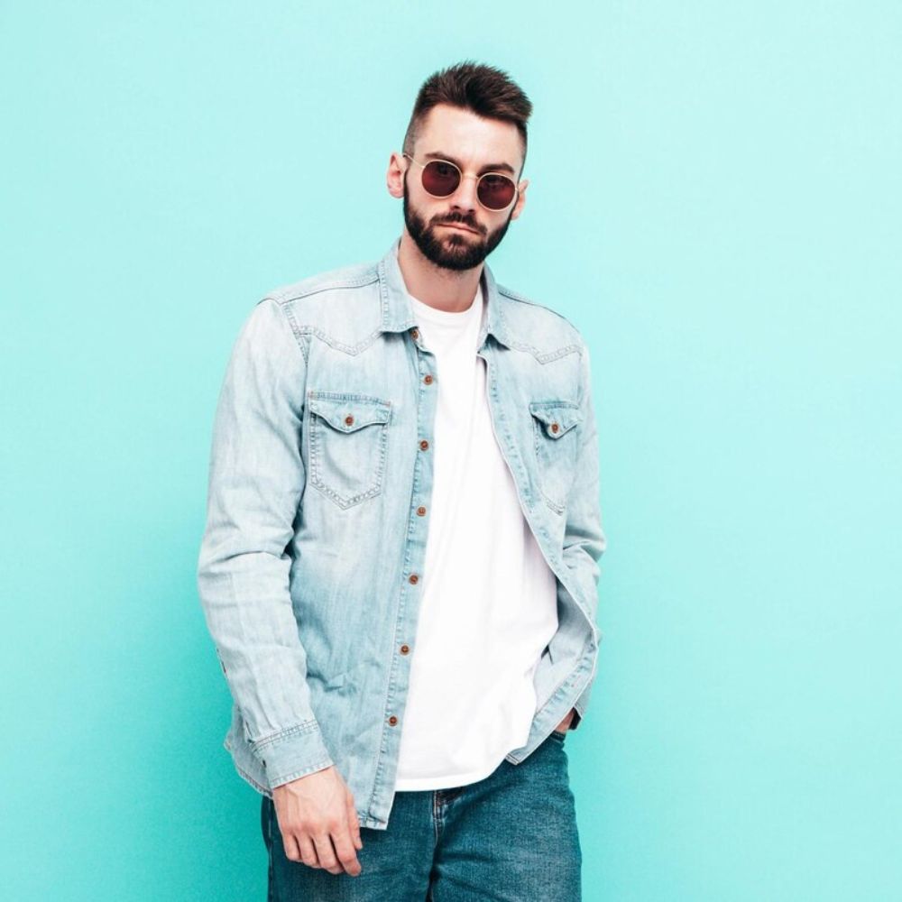 Man wearing a light blue denim jacket over a white shirt on a light blue background