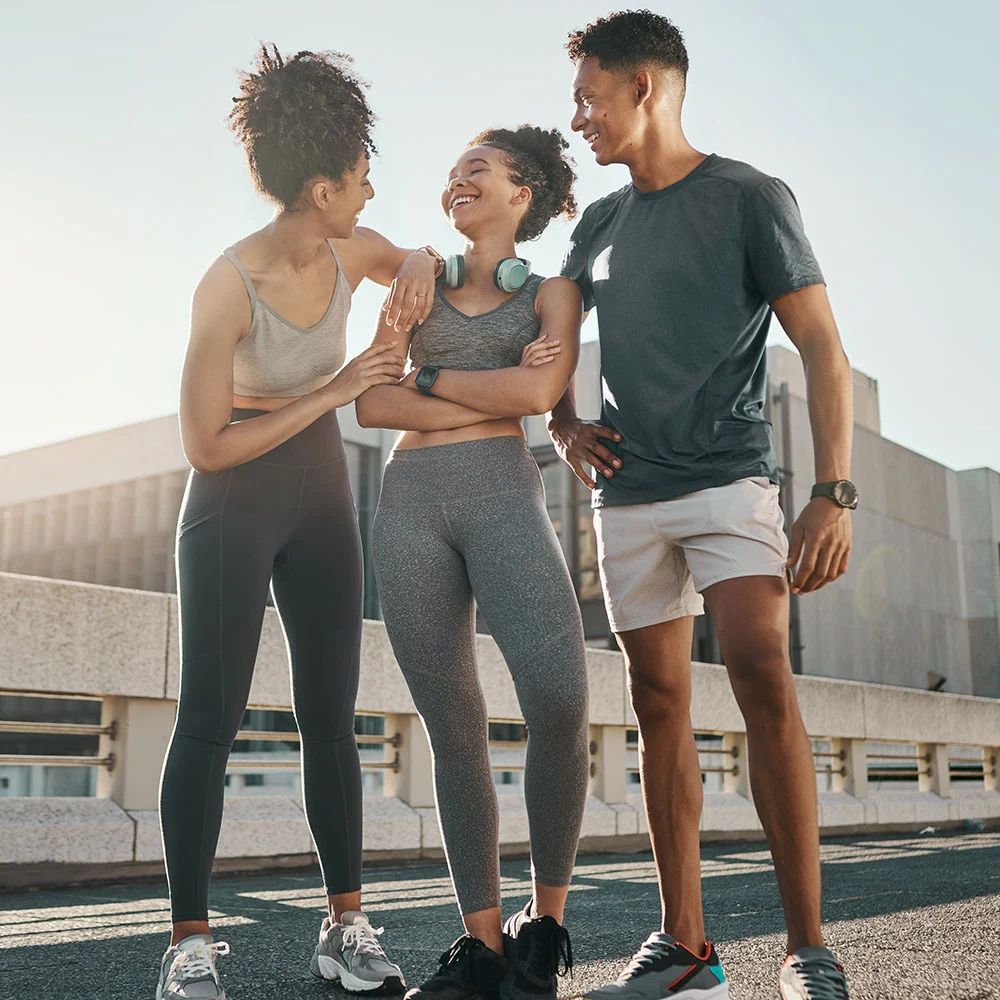 Three people in athletic wear standing together outdoors with a building in the background