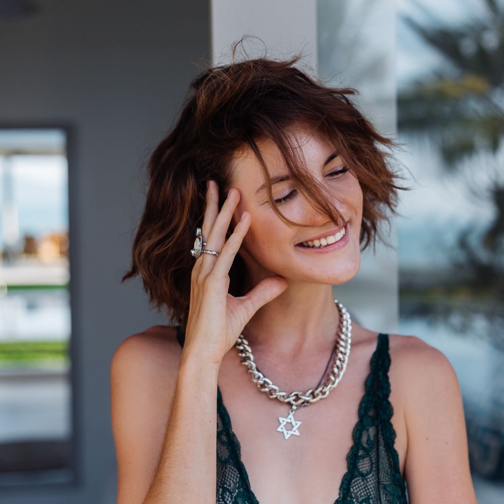 Woman wearing a necklace with a star pendant, smiling outdoors.